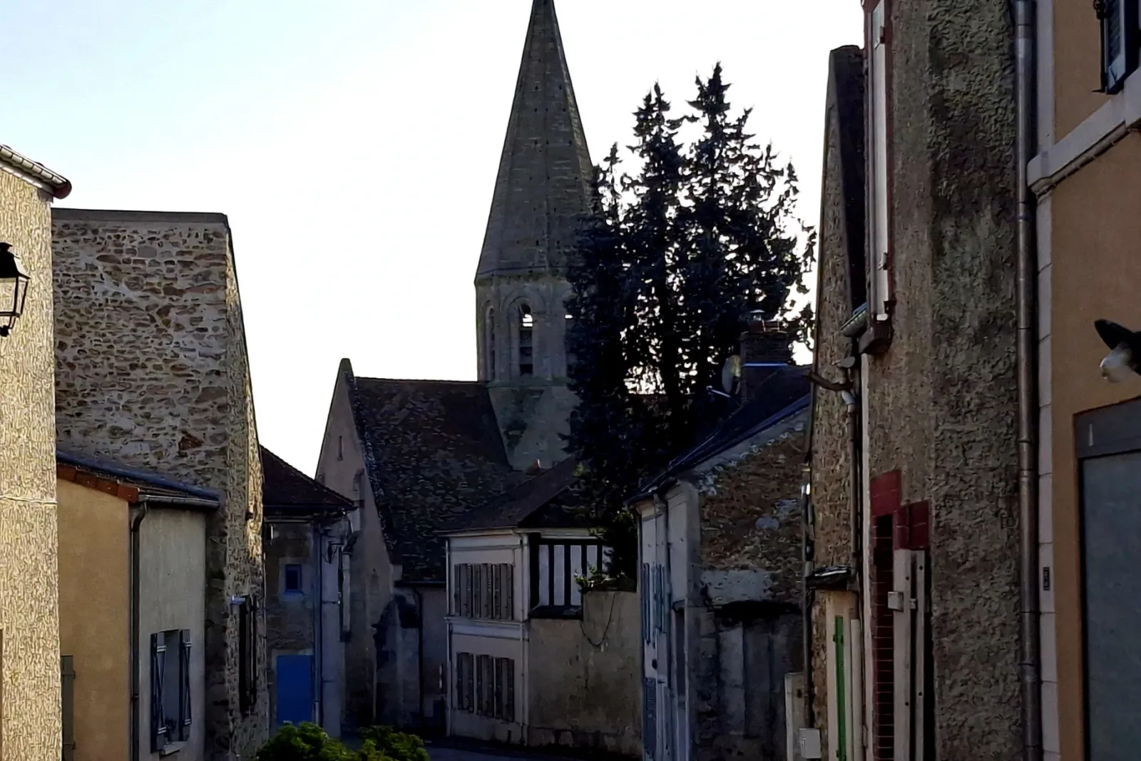 La rue qui monte vers l'église Sainte-Geneviève de Feucherolles, son clocher en flèche entre les maisons de meulière